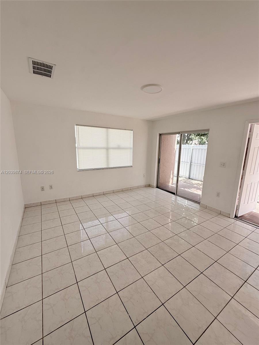 A bright, empty room features white walls, light-colored tile flooring, a window, and sliding doors — 2645 SW 28th Ct # 2645, Miami FL 33133, MIAMI, FL