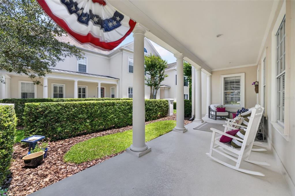 A covered porch features white columns, rocking chairs, and a manicured hedge in the yard — 331 CELEBRATION BOULEVARD, CELEBRATION, FL
