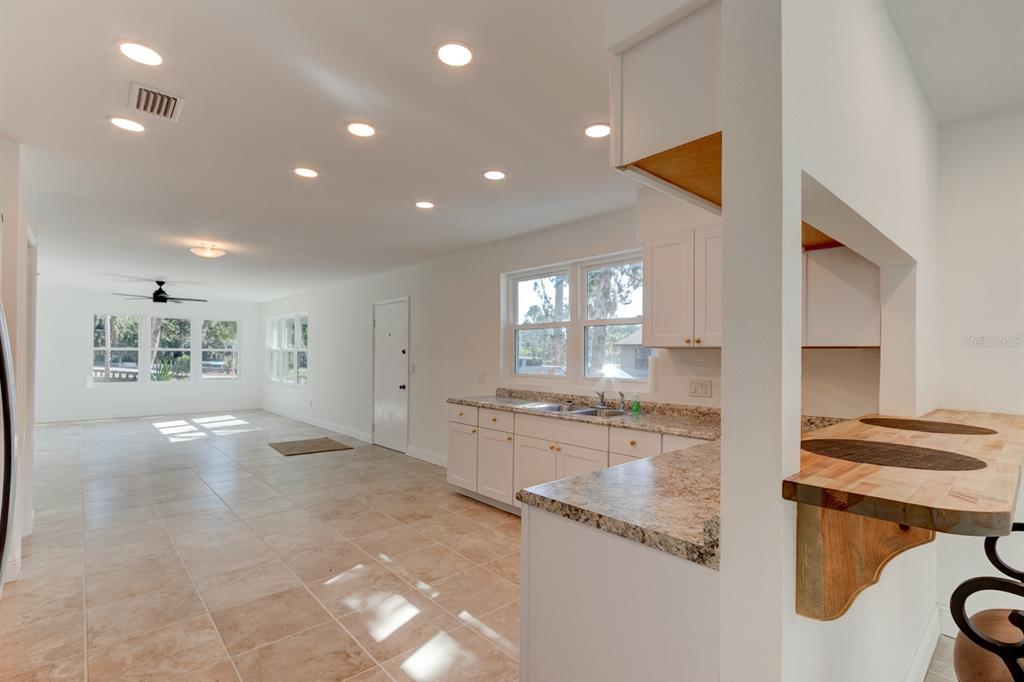 A kitchen with white cabinets and granite countertops opens into a bright, tiled living area — 4 MAIN STREET, PORT ORANGE, FL