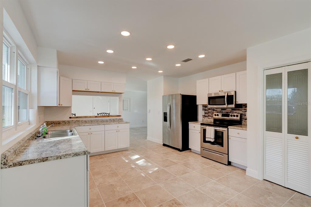 A kitchen with white cabinets, granite countertops, stainless steel appliances, and light tile flooring — 4 MAIN STREET, PORT ORANGE, FL