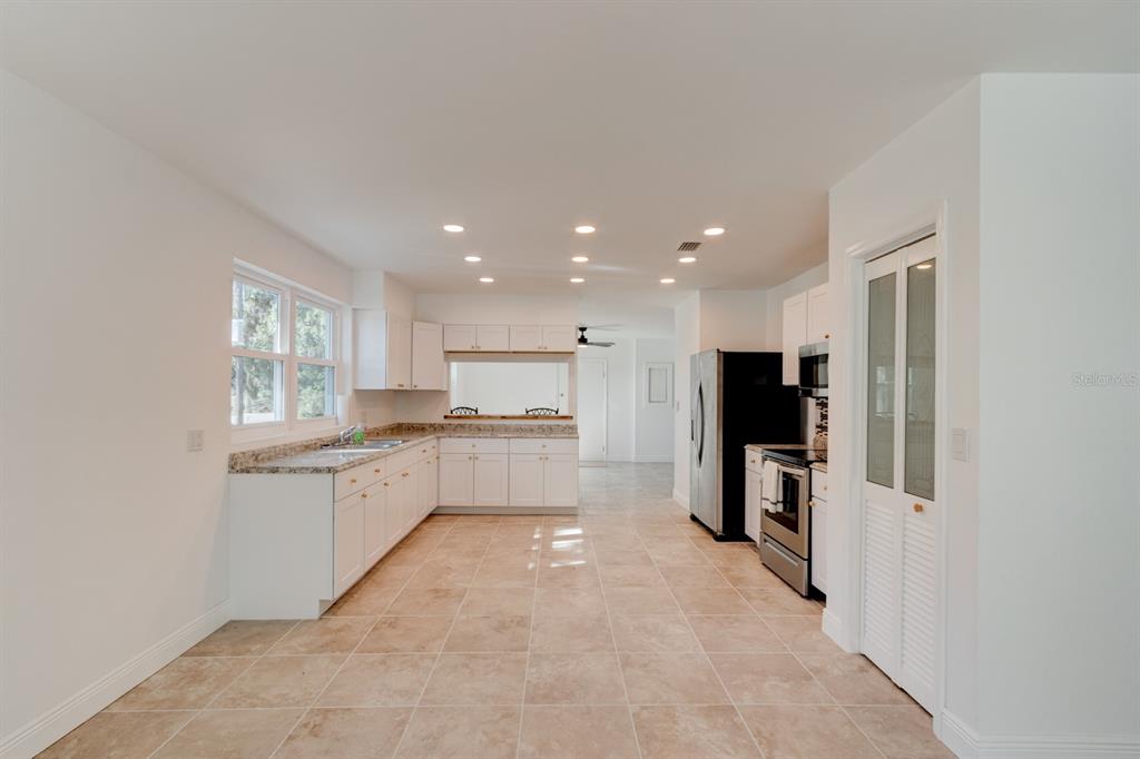 A kitchen features white cabinets, granite countertops, stainless steel appliances, and light tile flooring — 4 MAIN STREET, PORT ORANGE, FL