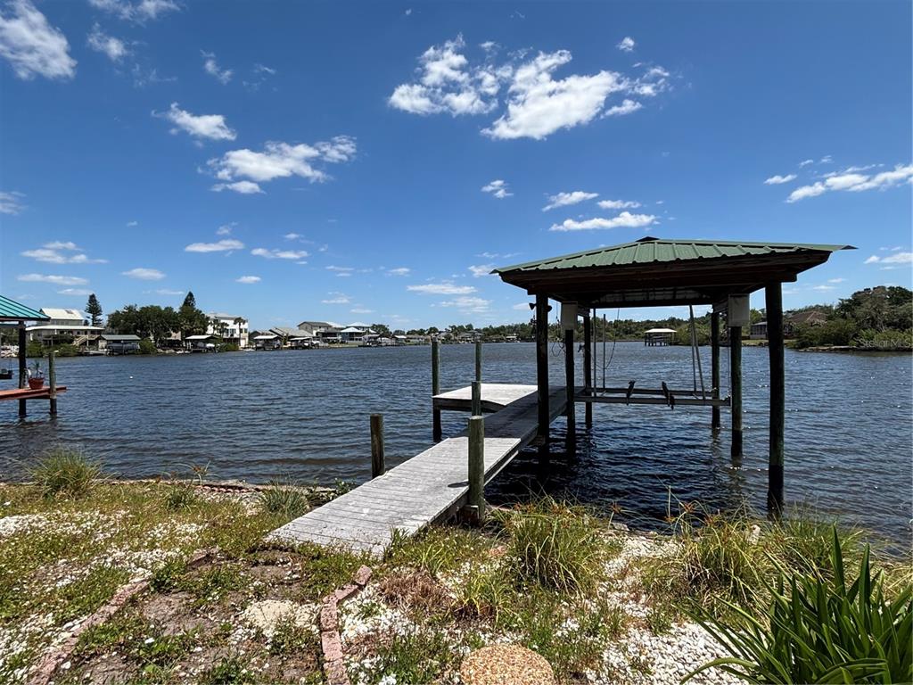 A wooden dock with a covered boat lift extends into a lake under a sky — 9922 ALAVISTA DRIVE, GIBSONTON, FL