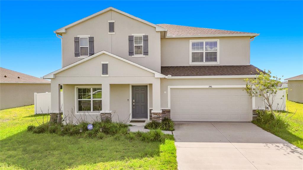 A two-story suburban house features a beige stucco exterior, a two-car garage, and shutters — 246 ZIRCON ROAD, KISSIMMEE, FL