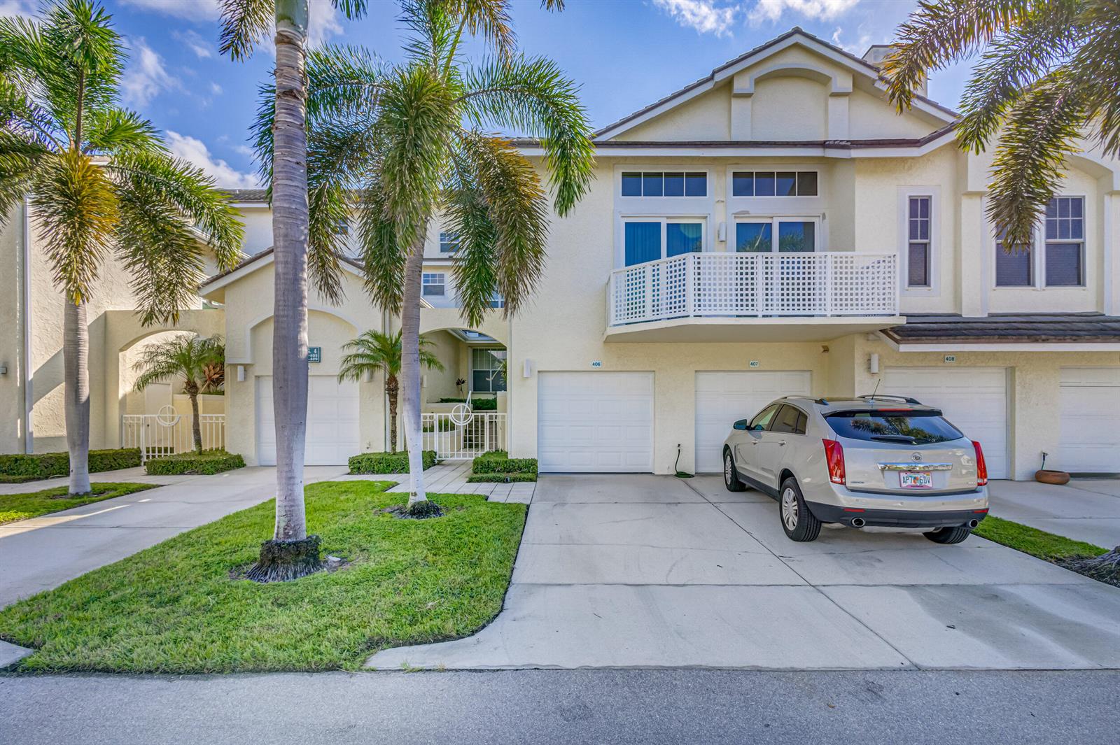 A multi-story townhouse exterior features a beige stucco facade, white garage doors, and palm trees — 406 Mainsail Circle, Jupiter FL 33477, JUPITER, FL
