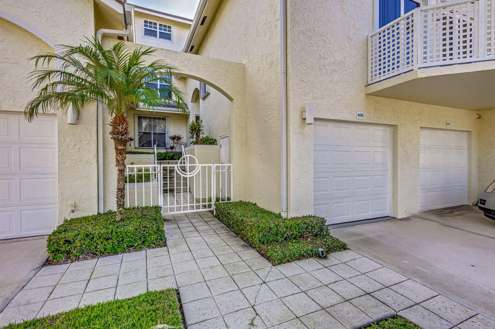 An exterior view of a multi-unit building with white garage doors and a gated walkway — 406 Mainsail Circle, Jupiter FL 33477, JUPITER, FL