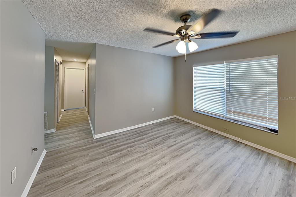 An empty room features gray walls, wood-look flooring, a ceiling fan, and a large window — 3352 MERCHANT TERRACE, DELTONA, FL