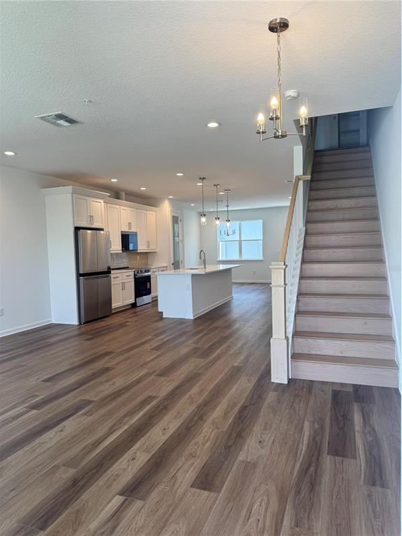 An open-concept kitchen features white cabinetry, a center island, and wood-look flooring near stairs — 1888 CROWNCREST DRIVE, APOPKA, FL