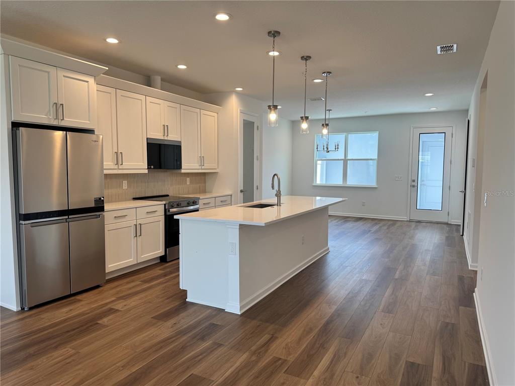 A modern kitchen features white cabinetry, stainless steel appliances, a center island, and wood flooring — 1888 CROWNCREST DRIVE, APOPKA, FL