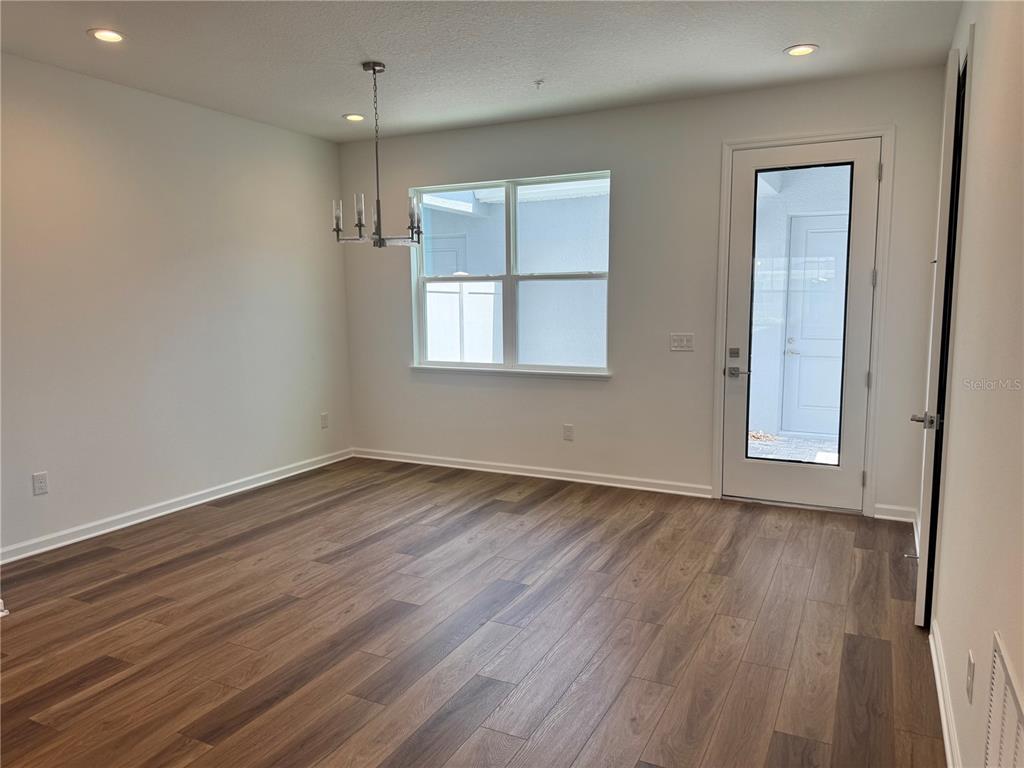 An empty dining room features wood-look flooring, a modern chandelier, and a glass-paneled exterior door — 1888 CROWNCREST DRIVE, APOPKA, FL