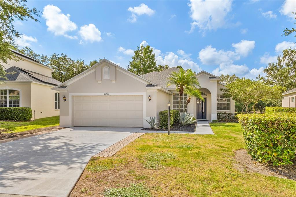 A single-story beige house with a two-car garage and a landscaped front yard — 14243 CATTLE EGRET PLACE, BRADENTON, FL