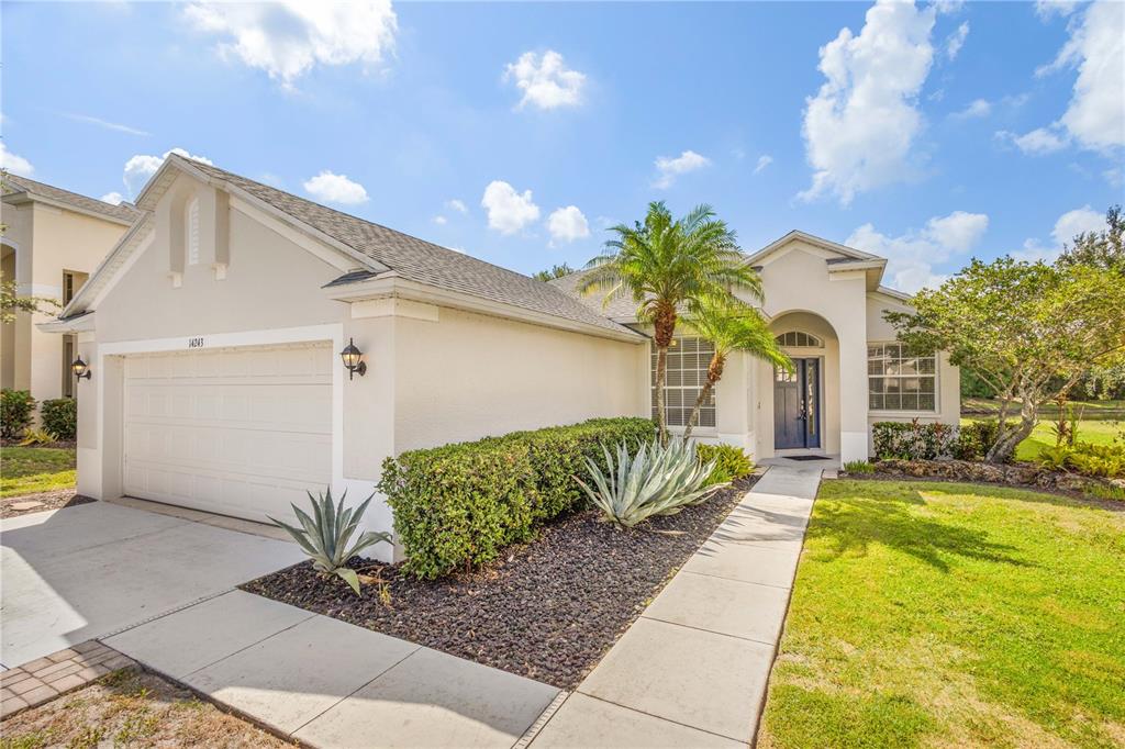 A single-story house with a two-car garage, a palm tree, and a landscaped front yard — 14243 CATTLE EGRET PLACE, BRADENTON, FL