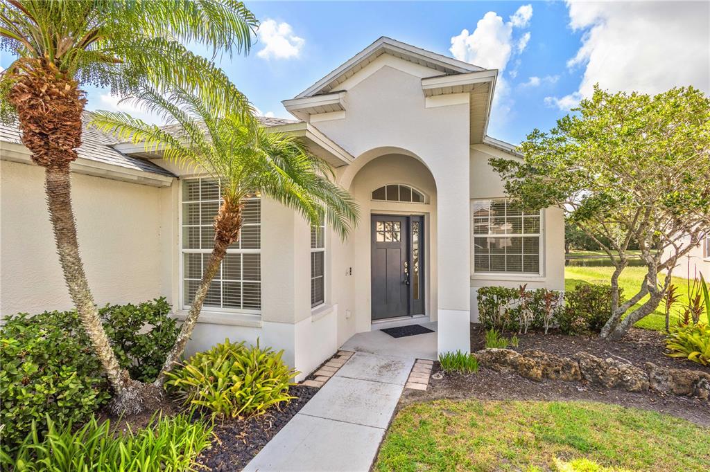 A single-story house exterior features a gray front door, arched entryway, and palm trees — 14243 CATTLE EGRET PLACE, BRADENTON, FL