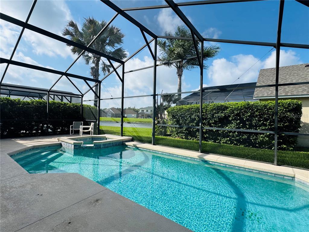 A swimming pool and spa are enclosed within a screened lanai overlooking a grassy yard — 4795 CUMBRIAN LAKES DRIVE, KISSIMMEE, FL