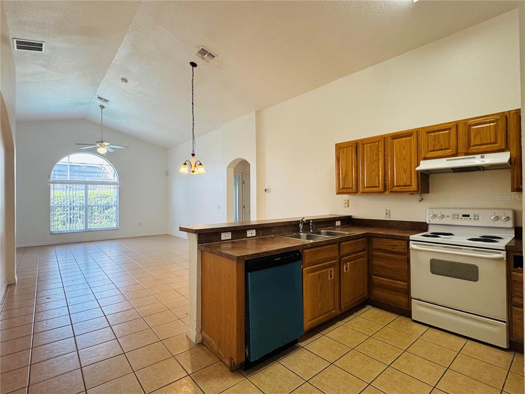 A kitchen with oak cabinets and tile floors opens to a living area with vaulted ceilings — 4795 CUMBRIAN LAKES DRIVE, KISSIMMEE, FL