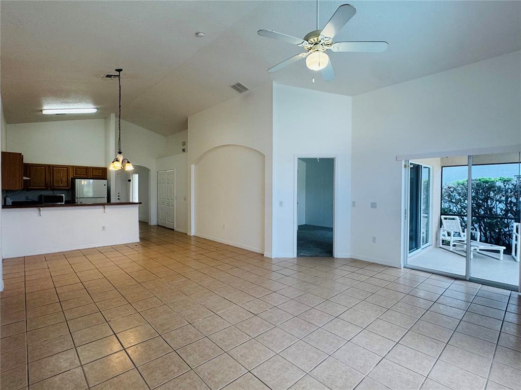 An open-concept living area features tile flooring, a kitchen with wood cabinets, and sliding doors — 4795 CUMBRIAN LAKES DRIVE, KISSIMMEE, FL