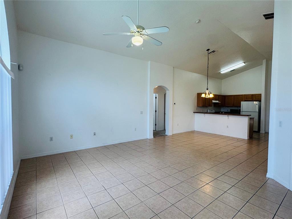 A spacious living room with tile flooring leads to an open kitchen with wooden cabinets — 4795 CUMBRIAN LAKES DRIVE, KISSIMMEE, FL