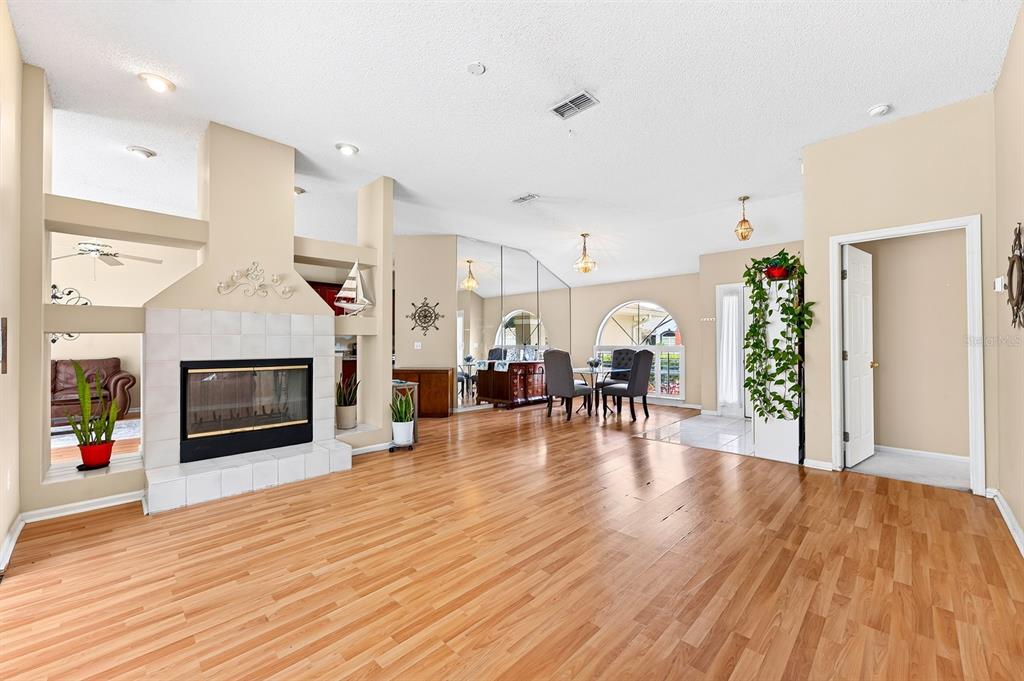 A living room with light wood flooring, a white tiled fireplace, and a dining area — 259 SILK BAY PLACE, LONGWOOD, FL