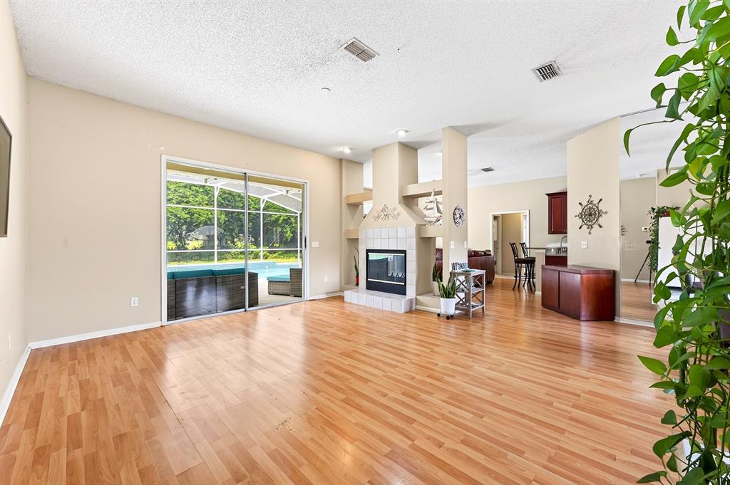 A living room with wood flooring, a central fireplace, and sliding doors leading to a pool — 259 SILK BAY PLACE, LONGWOOD, FL