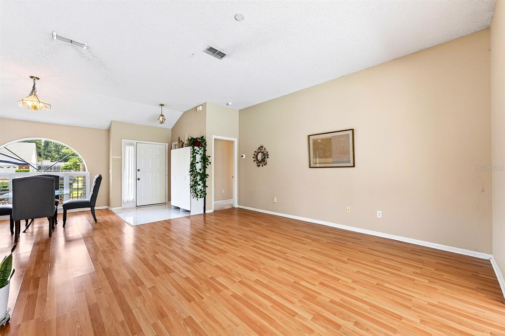A living room with light wood flooring, beige walls, and a white front door — 259 SILK BAY PLACE, LONGWOOD, FL