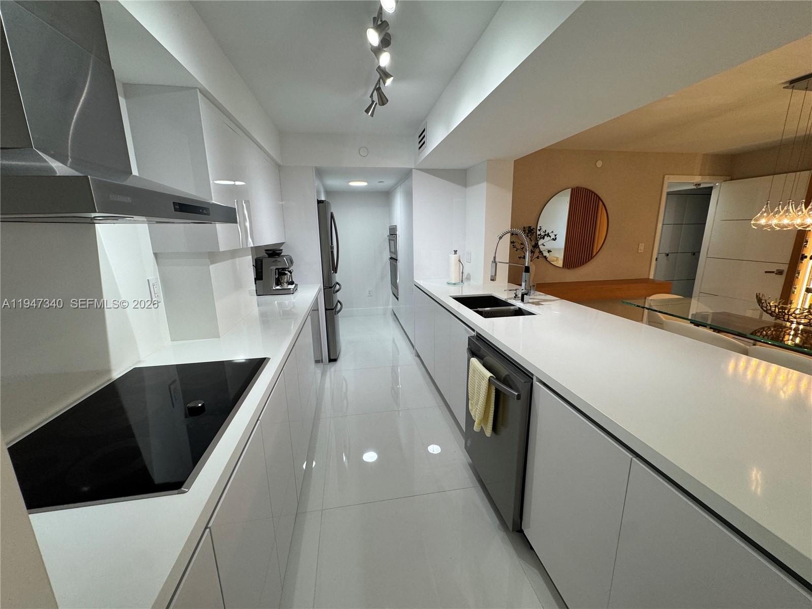 A modern galley kitchen features white cabinetry, white countertops, and stainless steel appliances — 5757 Collins Ave # 504, Miami Beach FL 33140, MIAMI BEACH, FL