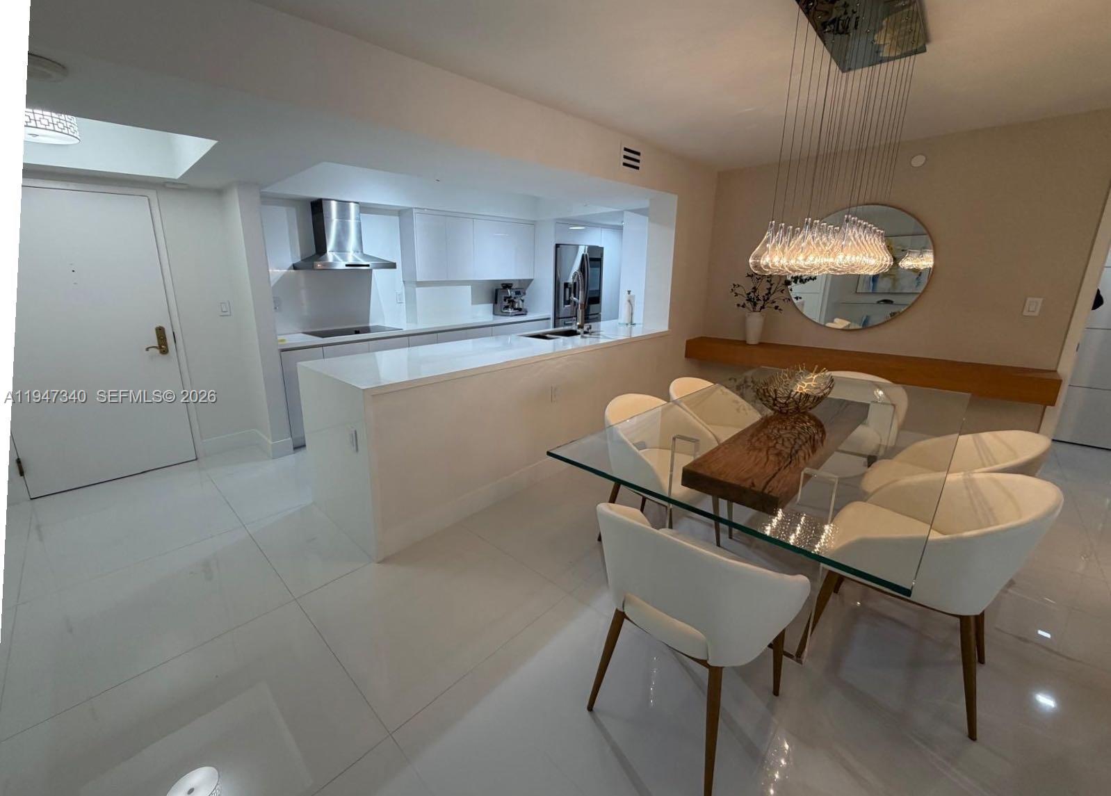A modern dining area features a glass table, white chairs, and an adjacent open kitchen — 5757 Collins Ave # 504, Miami Beach FL 33140, MIAMI BEACH, FL