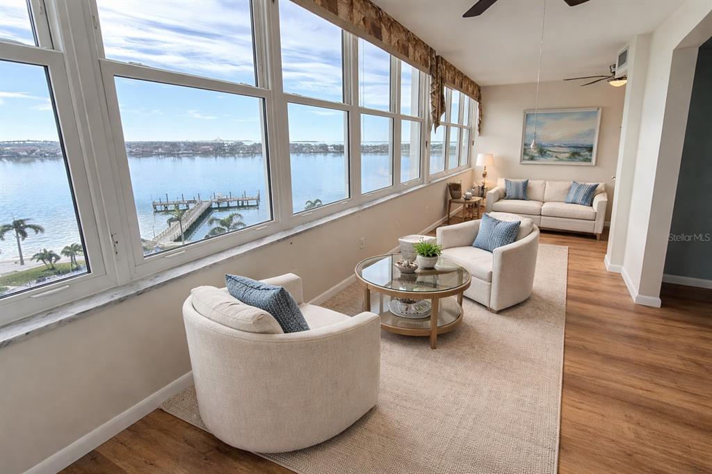 A sunroom features floor-to-ceiling windows with water views, light-colored furniture, and wood-look flooring — 5130 BRITTANY DRIVE S UNIT 807, ST PETERSBURG, FL