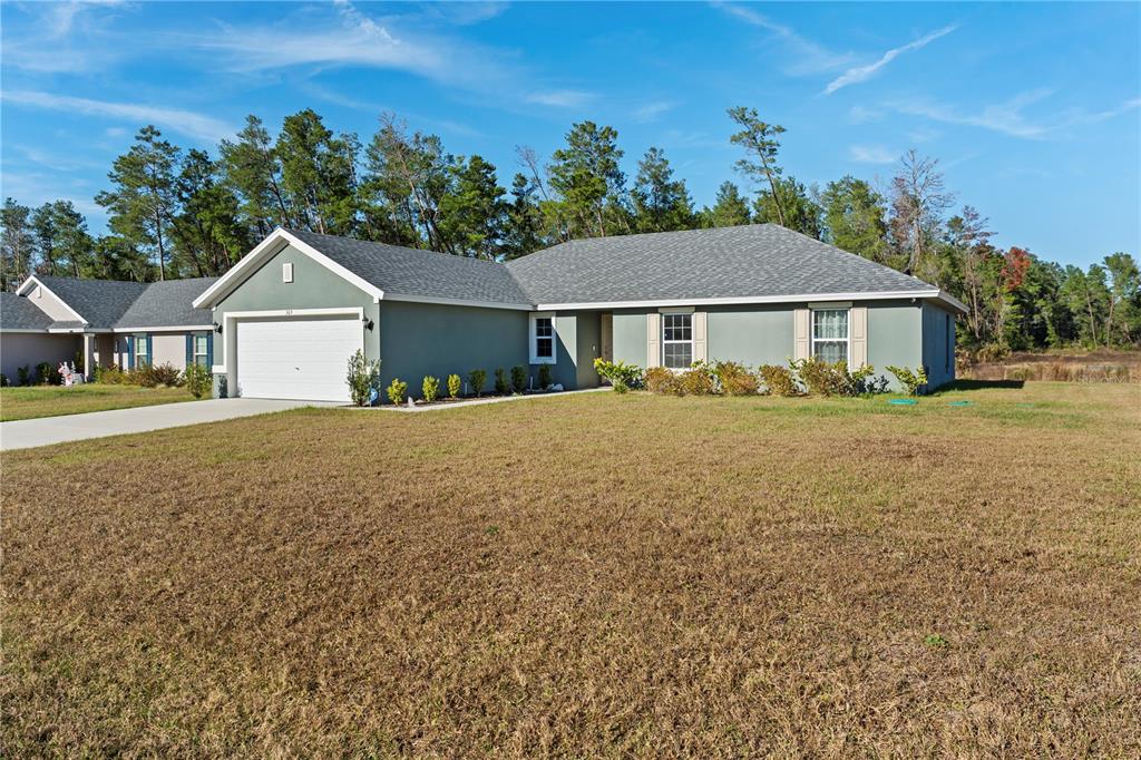 A single-story house with a white garage door and gray stucco exterior sits on grass — 369 MARION OAKS MANOR, OCALA, FL