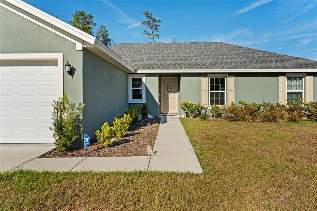 A single-story house with a green stucco exterior, a garage, and a concrete walkway — 369 MARION OAKS MANOR, OCALA, FL