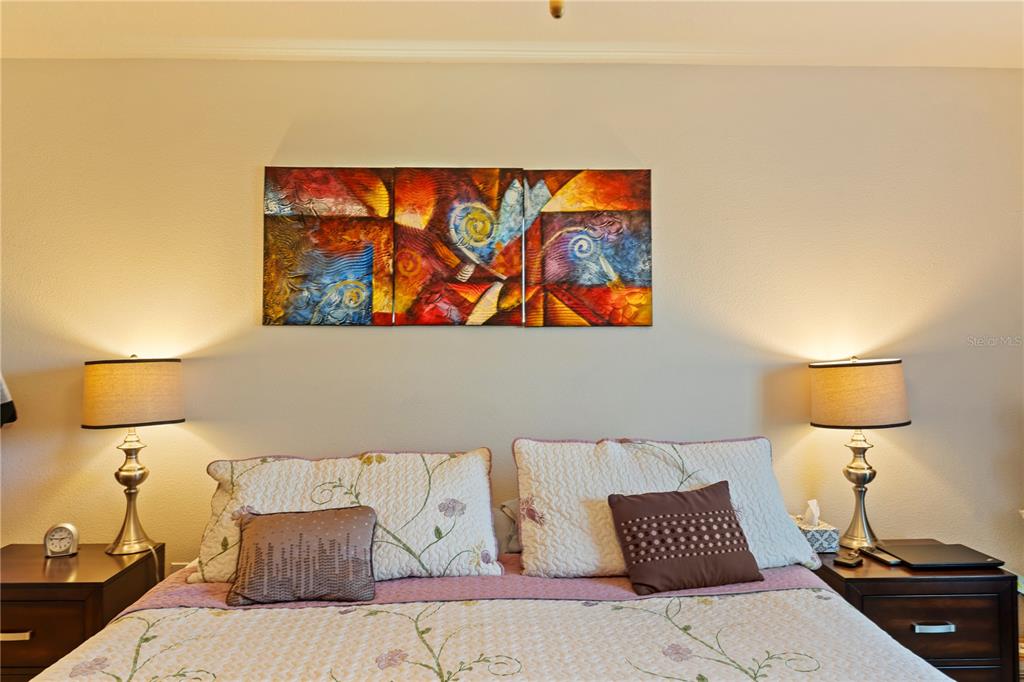 A bedroom features a bed with floral bedding, two nightstands with lamps, and abstract wall art — 369 MARION OAKS MANOR, OCALA, FL