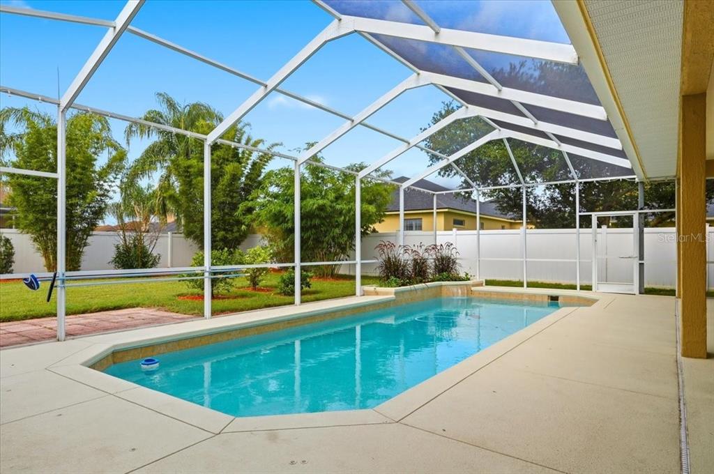 A swimming pool enclosed by a screened lanai sits in a backyard with a white fence — 2280 CHESTERFIELD CIRCLE, LAKELAND, FL