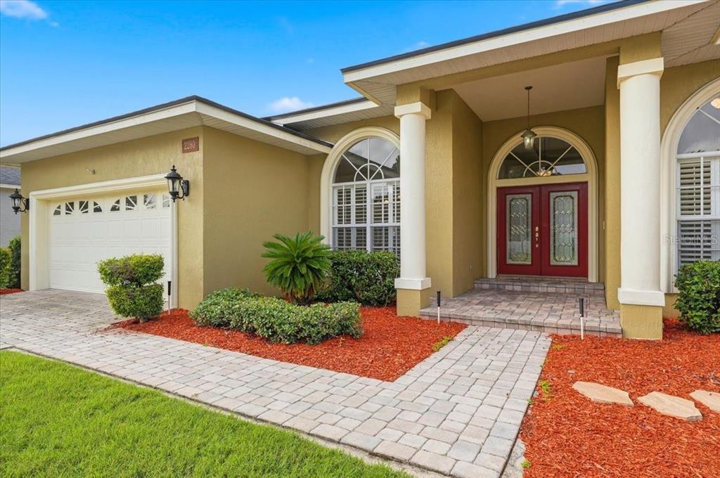 The exterior of a house features a paved walkway, red mulch, and red double doors — 2280 CHESTERFIELD CIRCLE, LAKELAND, FL