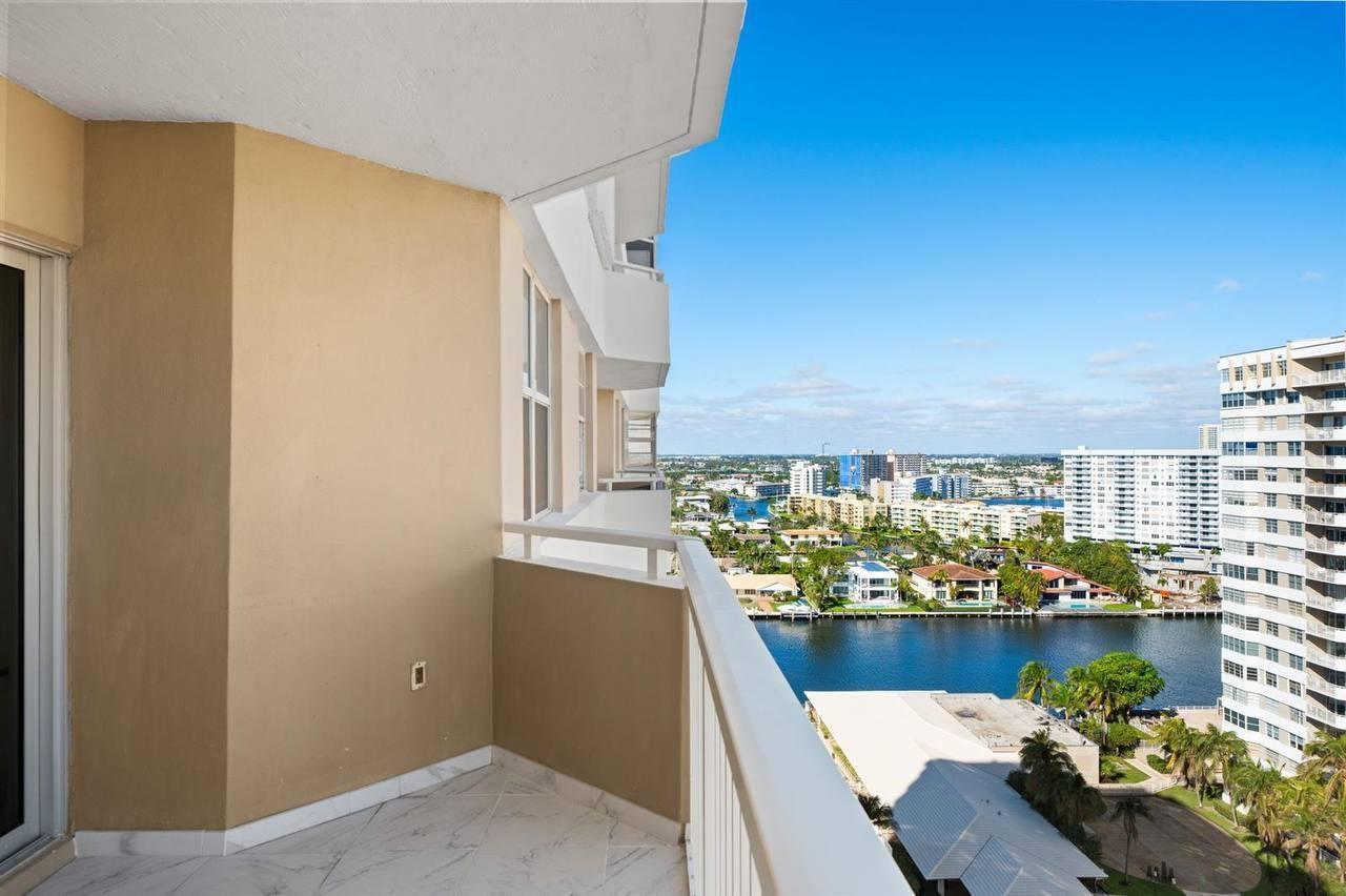 A high-rise balcony with white tile flooring overlooks a canal, surrounding buildings, and blue sky — 1985 S Ocean Drive # 16b, Hallandale Beach FL 33009, HALLANDALE BEACH, FL