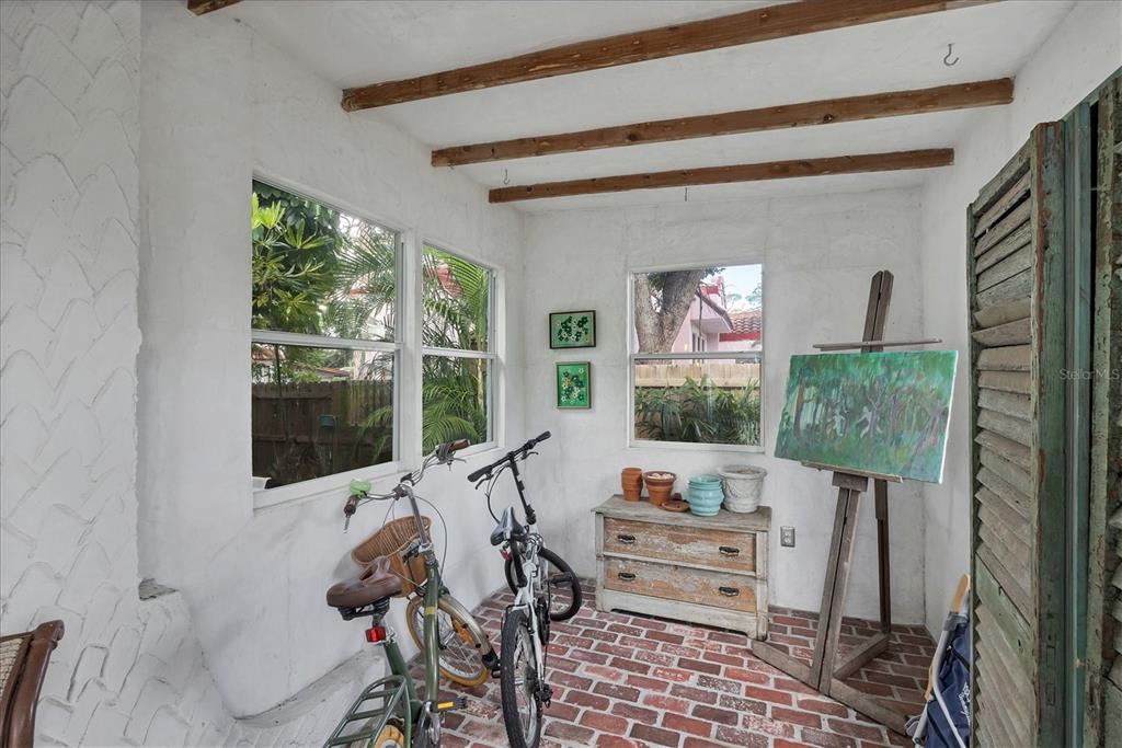 A sunroom features exposed wood ceiling beams, white textured walls, and a red brick floor — 1370 13TH STREET, SARASOTA, FL