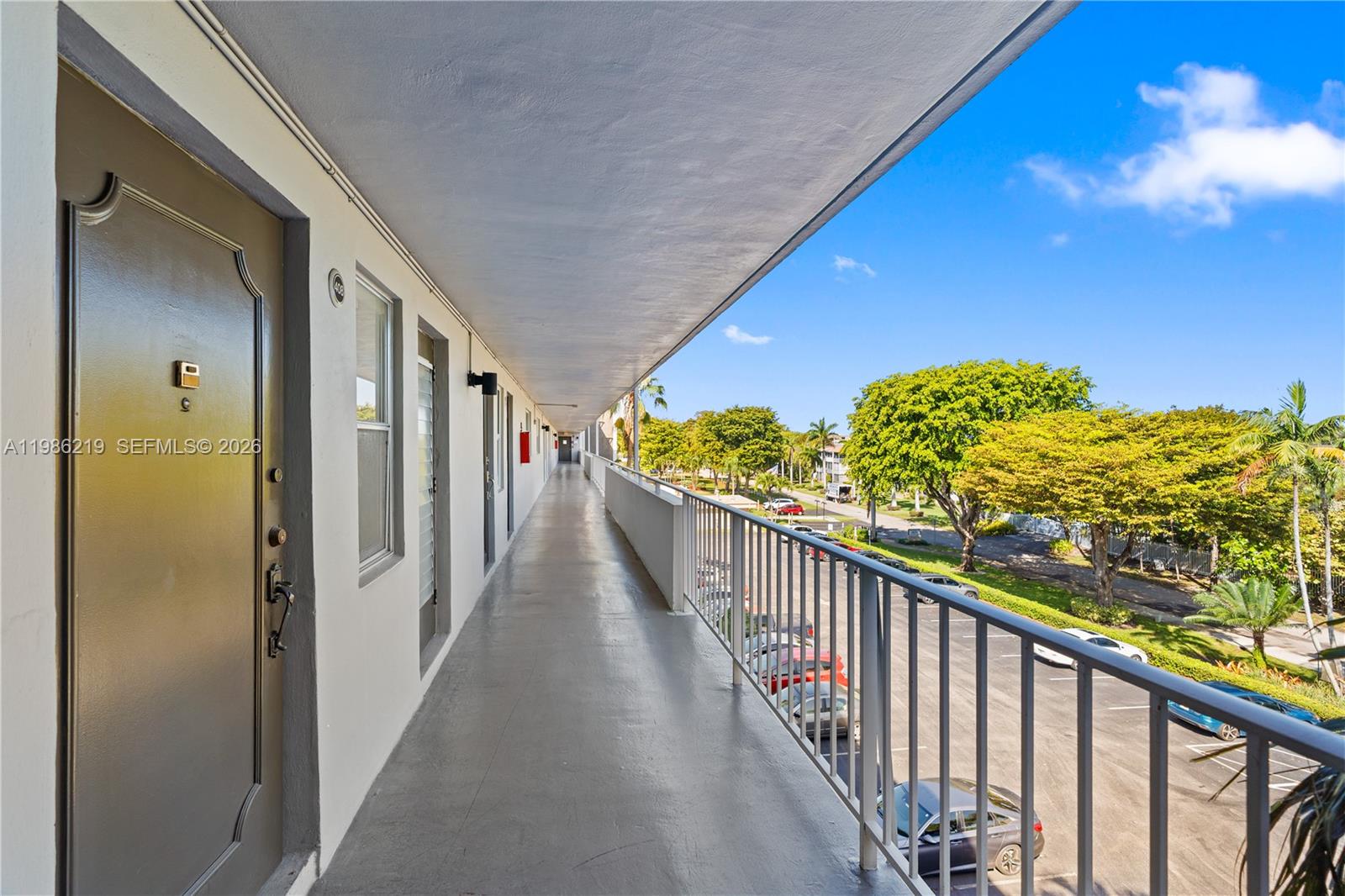 An outdoor apartment building walkway overlooks a parking lot with trees under a blue sky — 4800 Hillcrest Ln # 408, Hollywood FL 33021, HOLLYWOOD, FL