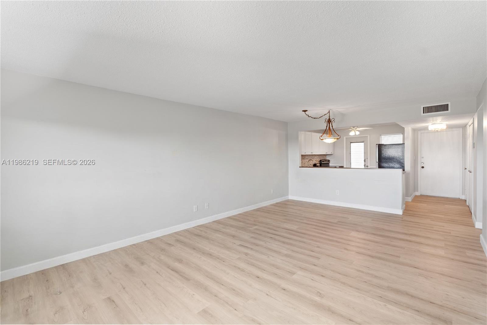 An empty living room features light wood-look flooring, gray walls, and an open kitchen pass-through — 4800 Hillcrest Ln # 408, Hollywood FL 33021, HOLLYWOOD, FL