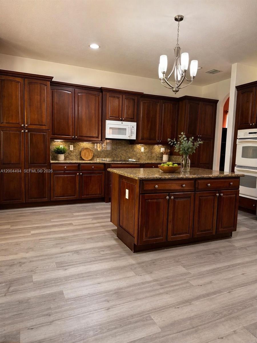 A kitchen features dark wood cabinets, granite countertops, a center island, and light wood flooring — 7441 SW 187th St, Cutler Bay FL 33157, CUTLER BAY, FL