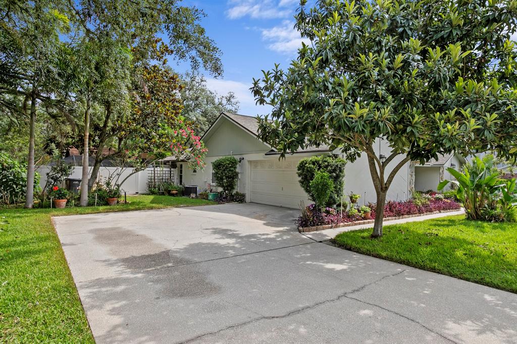 A concrete driveway leads to the garage of a single-story house with mature landscaping — 6314 E 112TH AVENUE, TAMPA, FL