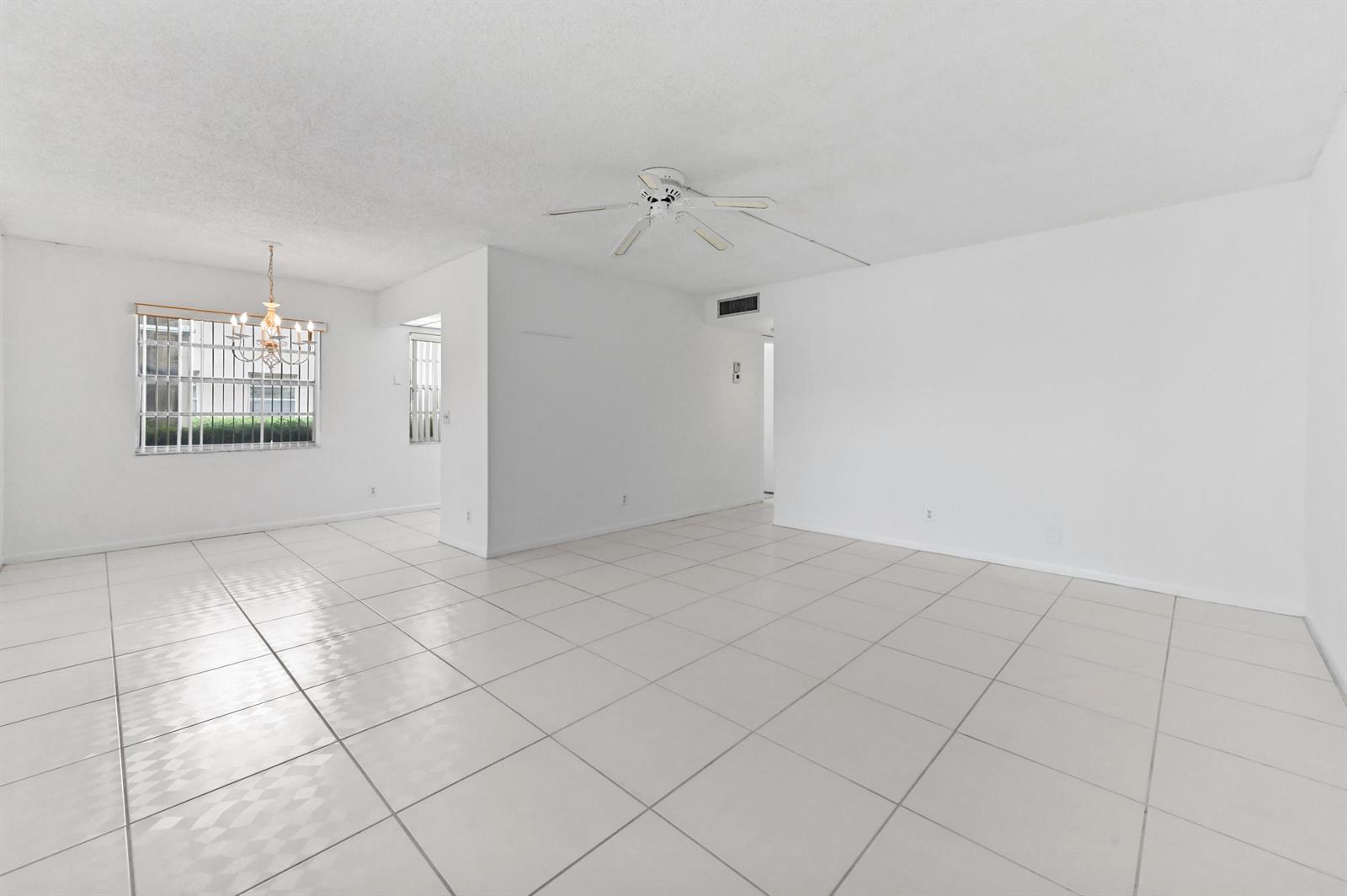 An empty living and dining area features white tile flooring, a ceiling fan, and windows — 346 Capri # H, Delray Beach FL 33484, DELRAY BEACH, FL