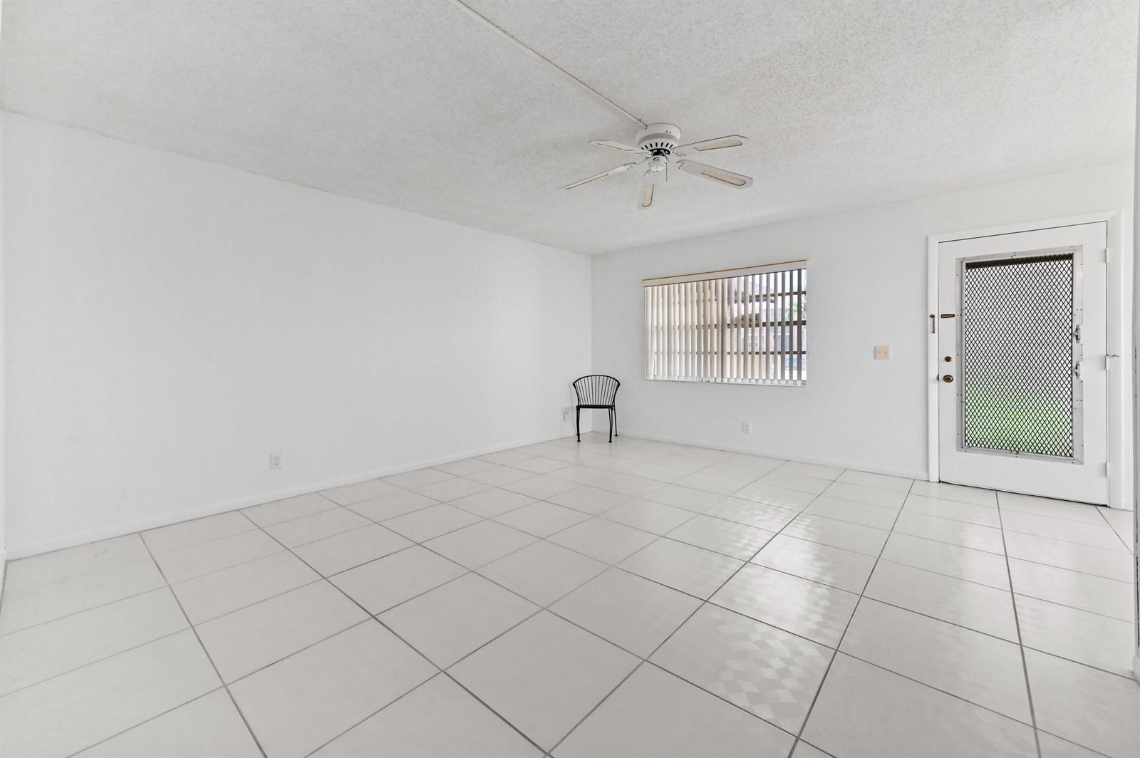 A bright, empty room features white tiled floors, white walls, a ceiling fan, and a door — 346 Capri # H, Delray Beach FL 33484, DELRAY BEACH, FL