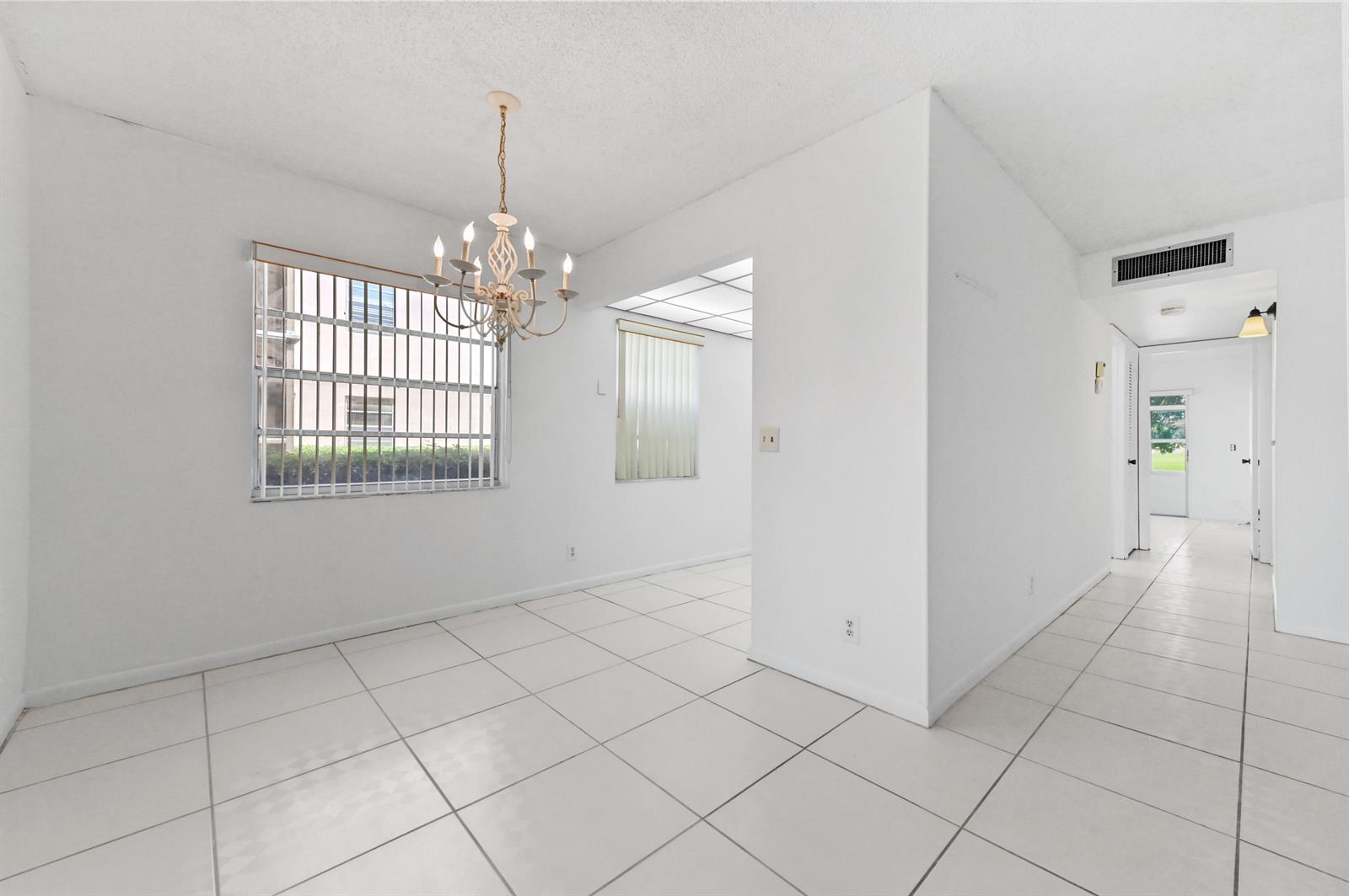 A dining area with white tile floors, a chandelier, and a hallway leading to a door — 346 Capri # H, Delray Beach FL 33484, DELRAY BEACH, FL