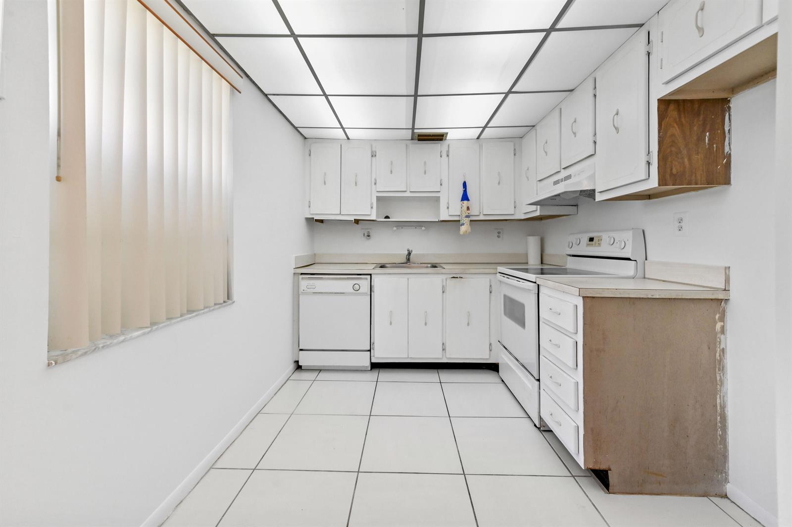 A white kitchen features tiled floors, a drop ceiling, and white cabinetry with an exposed side — 346 Capri # H, Delray Beach FL 33484, DELRAY BEACH, FL