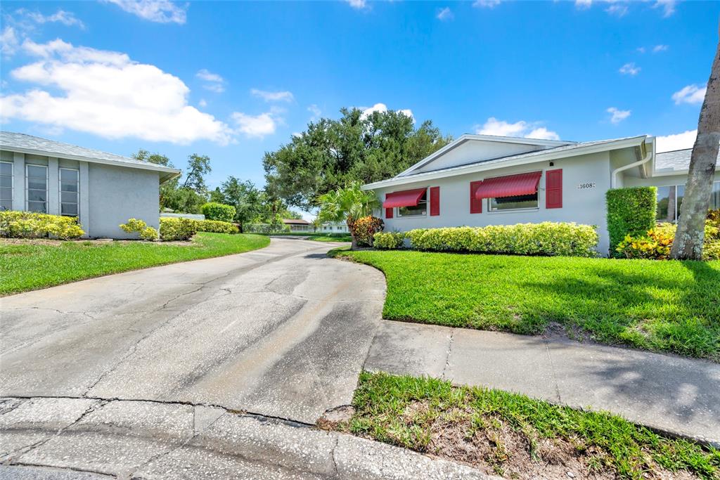 A single-story house with a concrete driveway, red window awnings, and a green lawn — 1608 WHITEBRIDGE DRIVE UNIT B, PALM HARBOR, FL