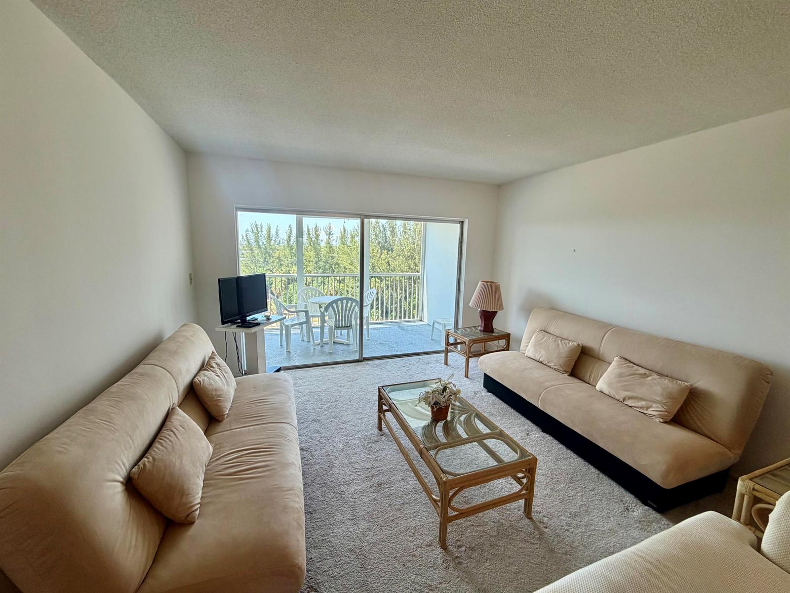 A living room features two beige sofas, a glass-top coffee table, and a balcony view — 3150 N Palm Aire Drive # 804, Pompano Beach FL 33069, POMPANO BEACH, FL