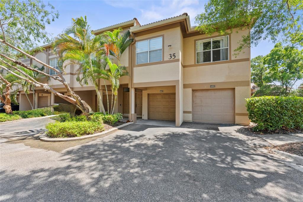 A two-story townhouse exterior features two garage doors, beige stucco walls, and palm trees — 603 ARBOR LAKE LN, TAMPA, FL