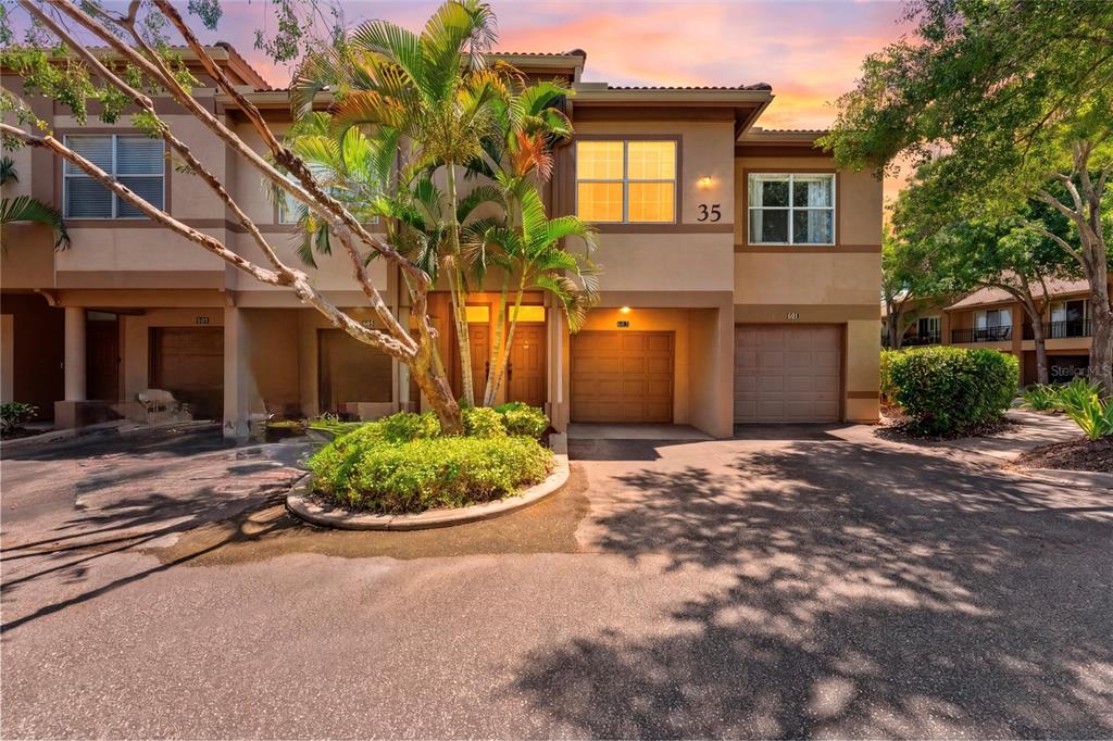 A two-story townhouse exterior features a palm tree, a small garden, and two garage doors — 603 ARBOR LAKE LN, TAMPA, FL