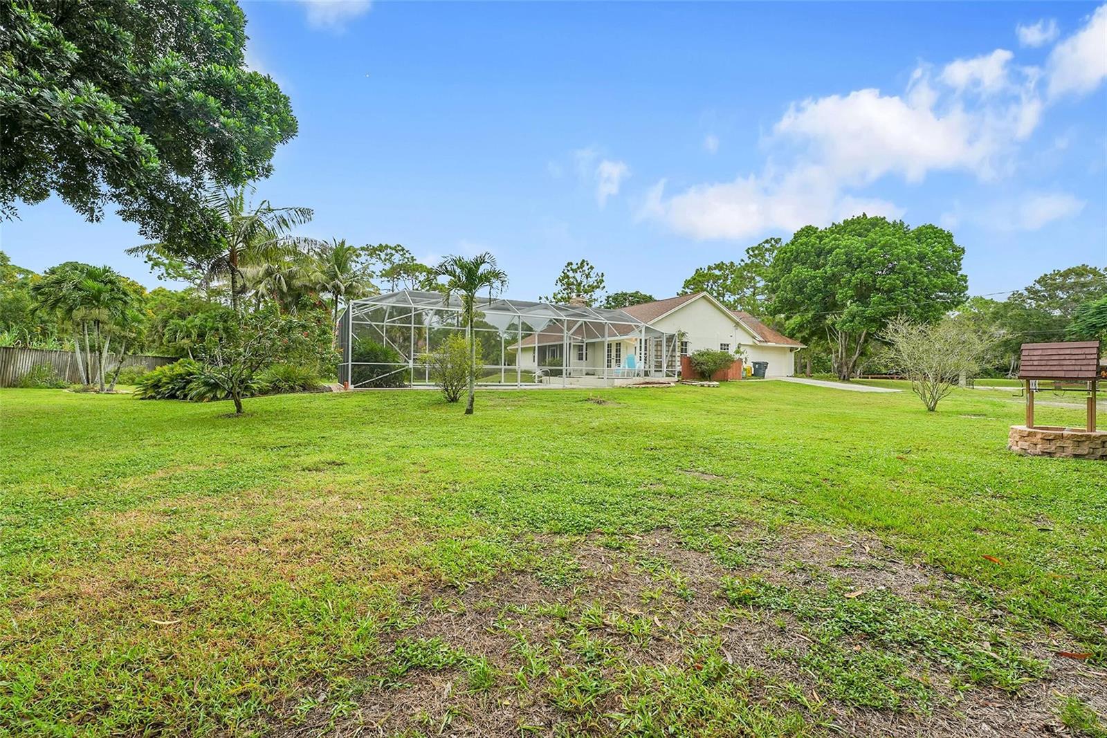 A backyard view of a house with a screened-in pool enclosure and a stone well — 18392 48th Avenue N, Loxahatchee FL 33470, LOXAHATCHEE, FL