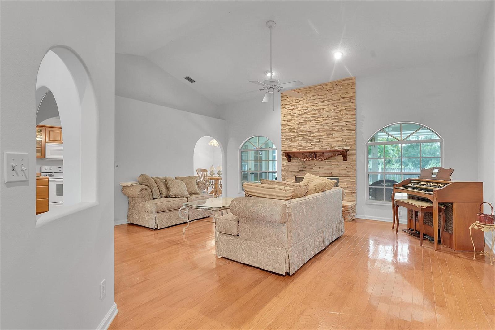 A living room features a stone fireplace, arched windows, hardwood floors, and a wooden organ — 18392 48th Avenue N, Loxahatchee FL 33470, LOXAHATCHEE, FL