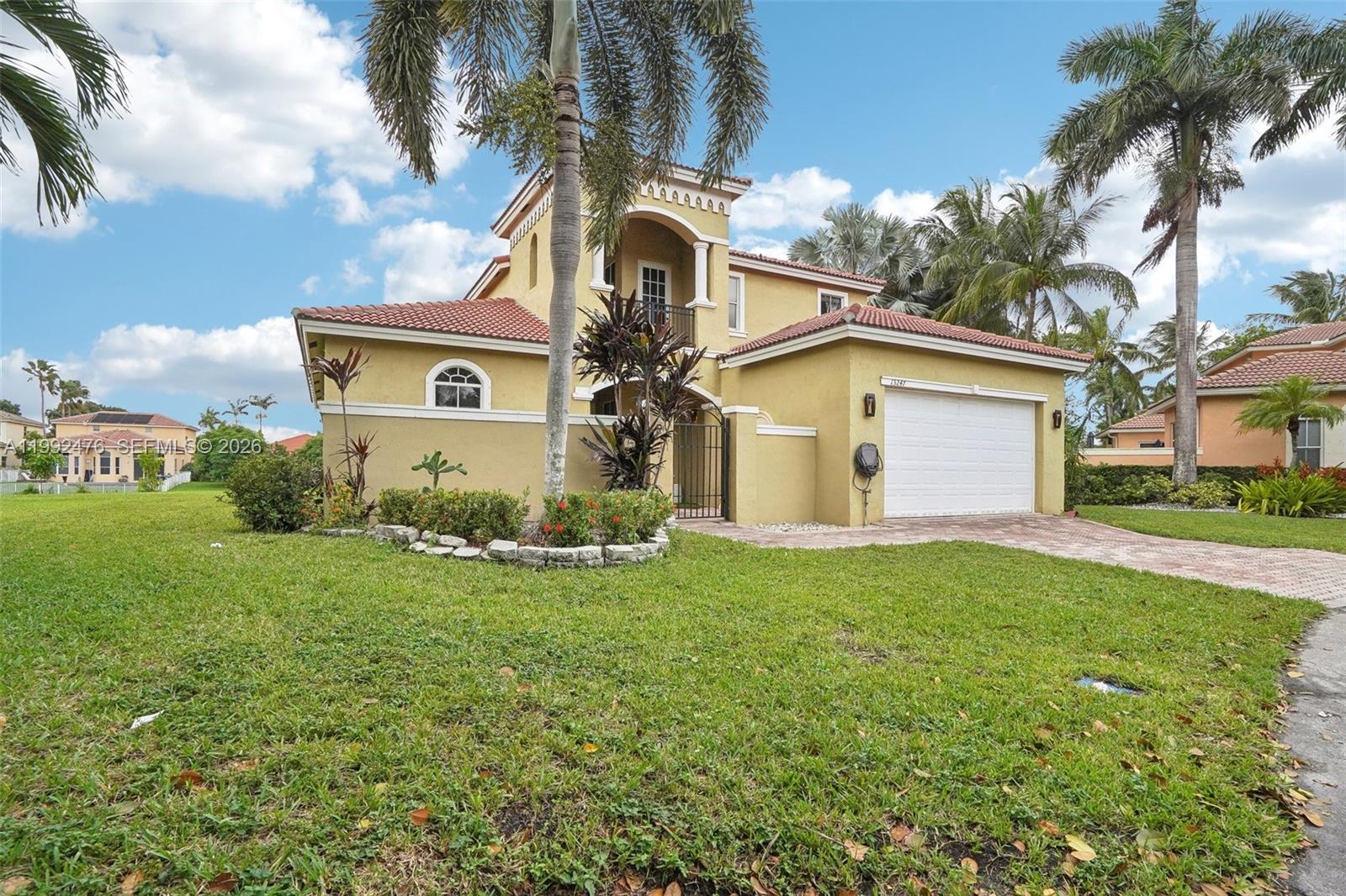 A two-story yellow stucco house features a tile roof, a garage, and palm trees — 13247 SW 26th St, Miramar FL 33027, MIRAMAR, FL
