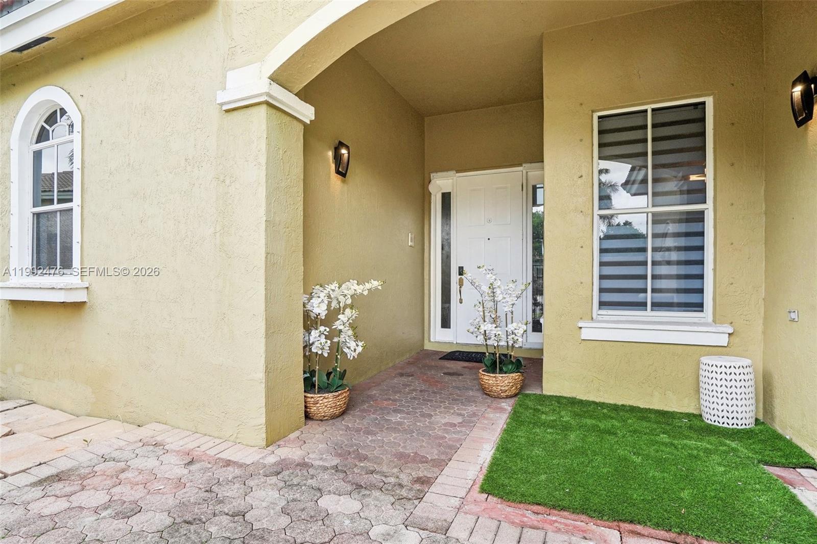 The front entrance features a white door, arched window, and potted plants on pavers — 13247 SW 26th St, Miramar FL 33027, MIRAMAR, FL