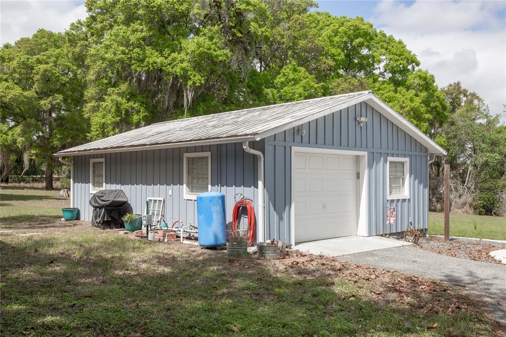A detached blue garage with a metal roof sits on a grassy lot with trees — 1905 MYRTLE LAKE AVENUE, FRUITLAND PARK, FL